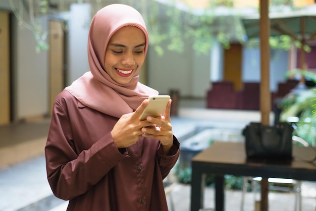 una mujer con hijab mira su teléfono y sonríe