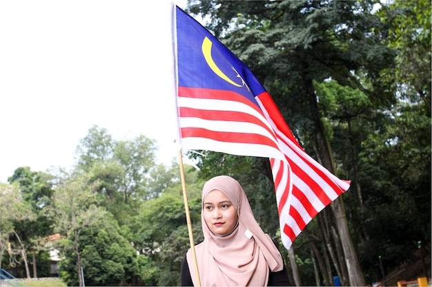 Mujer con hijab sosteniendo una bandera contra los árboles