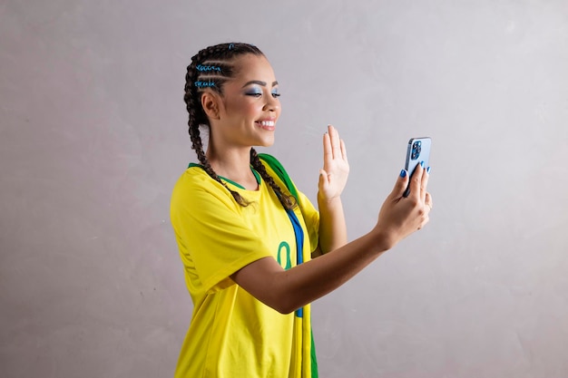 Mujer hincha brasileña animando a brasil en la copa del mundo 2022 en videollamada hablando con amigos de forma remota teléfono celular con tecnología de comunicación celular