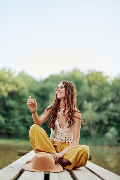 Una mujer hippie se sienta en un puente junto a un lago en un viaje por la naturaleza y sonríe con ropa ecológica El concepto de ecoactivista y conservación de la naturaleza Foto de alta calidad