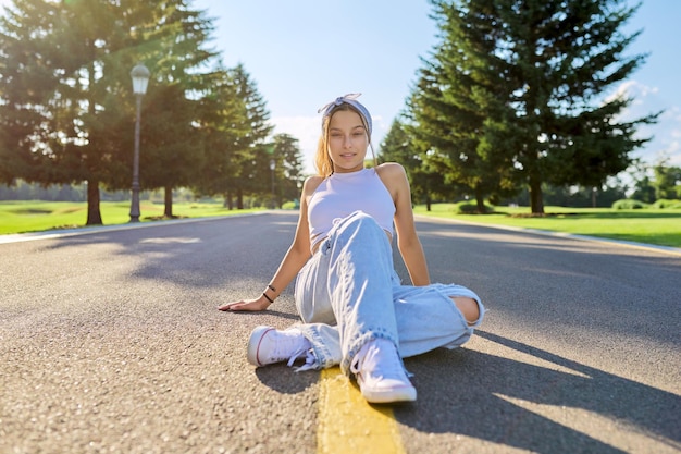 Mujer hipster adolescente de moda sentada en la carretera en el parque