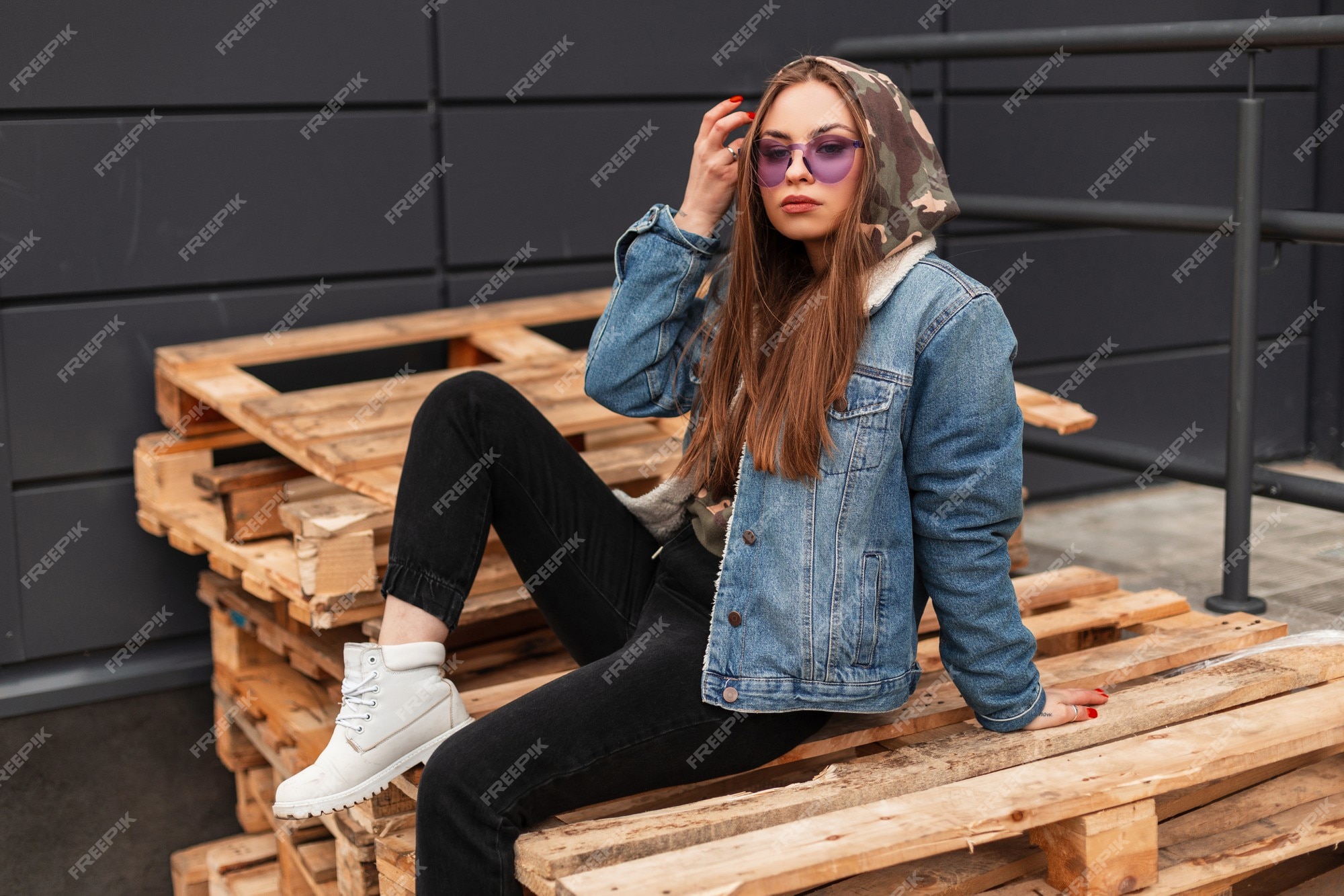 Mujer con estilo joven fresco urbano en ropa juvenil casual de moda gafas moradas de moda posa en la ciudad. modelo de moda chica glamorosa se sienta en palets de