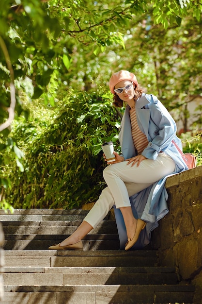 Mujer hipster sentada en un banco de piedra al aire libre disfrutando del té y el sol