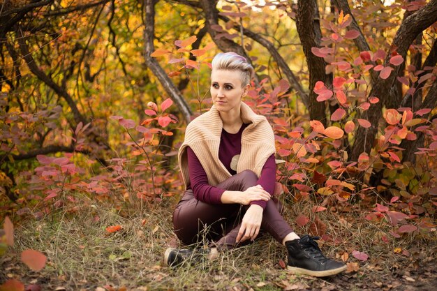 Mujer hipster sentada en el fondo del bosque otoñal con árboles dorados y rojos