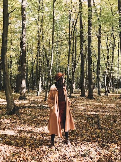 Mujer hipster con sombrero y abrigo viajando en el bosque soleado de otoño con hojas de otoño Chica viajera elegante explorando bosques de otoño disfrutando del día soleado