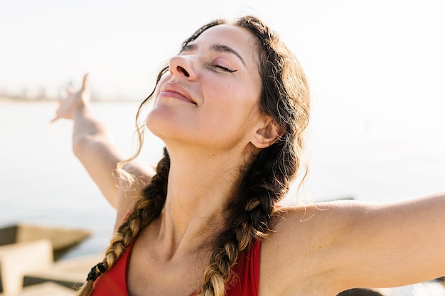 Foto mujer hispana adulta joven que respira aire fresco de pie en la playa en verano - retrato de mujer hispana deportiva relajante junto al mar - concepto de estilo de vida de bienestar y salud