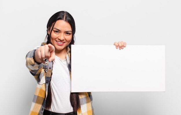 Mujer hispana apuntando a la cámara con una sonrisa satisfecha, confiada y amistosa, eligiéndote