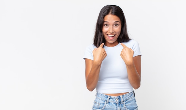 Mujer hispana bastante delgada que se siente feliz y apuntando a sí misma con un emocionado