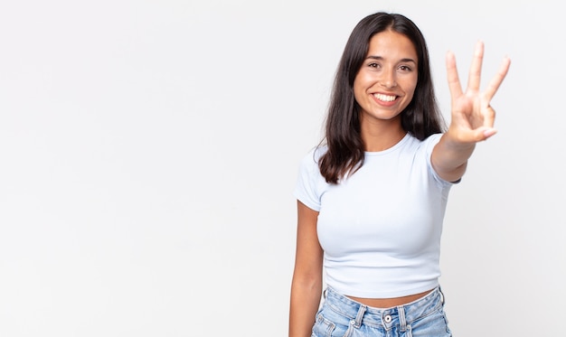 Mujer hispana bastante delgada sonriendo y mirando amigable, mostrando el número tres