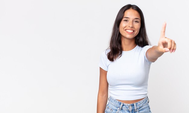 Mujer hispana bastante delgada sonriendo y mirando amigable, mostrando el número uno