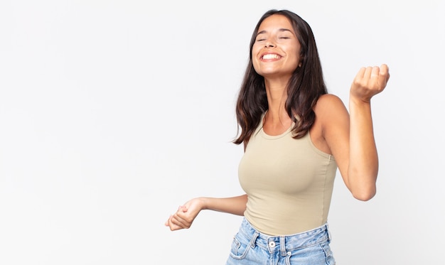 Mujer hispana bastante delgada sonriendo, sintiéndose despreocupada y bailando y escuchando música