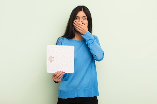 Mujer hispana bonita joven que cubre la boca con las manos con una sorpresa. concepto de rompecabezas