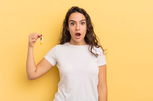 Mujer hispana bonita joven que parece muy conmocionada o sorprendida. concepto de termómetro