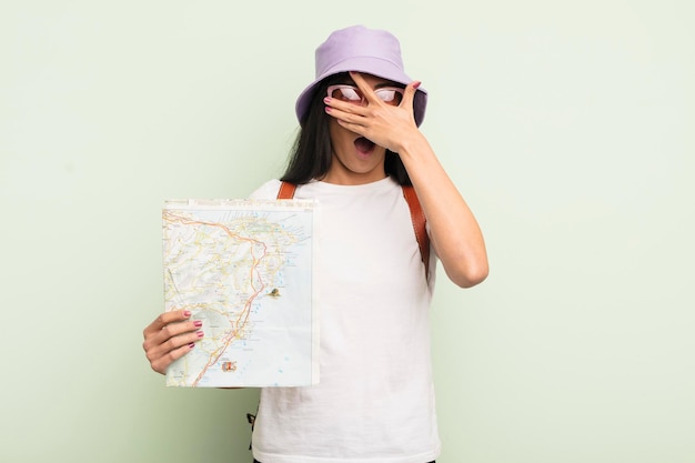 Mujer hispana bonita joven que parece sorprendida asustada o aterrorizada cubriendo la cara con el turista de mano y el concepto de mapa