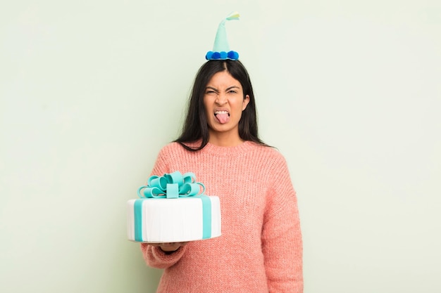 Mujer hispana bonita joven que se siente disgustada e irritada y saca la lengua concepto de pastel de cumpleaños