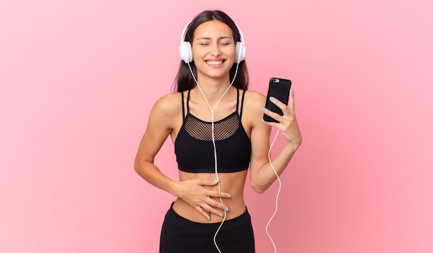 Mujer hispana de fitness riendo a carcajadas de una broma hilarante con auriculares y un teléfono