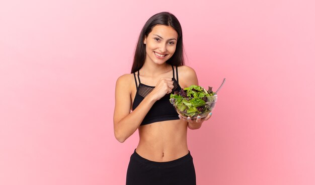 Mujer hispana fitness sintiéndose feliz y enfrentando un desafío o celebrando y sosteniendo una ensalada