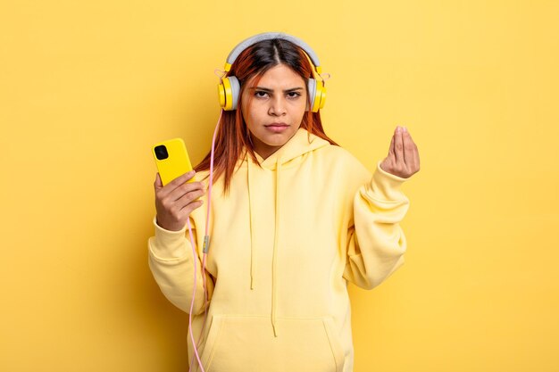 Mujer hispana haciendo capice o gesto de dinero diciéndole que pague auriculares y concepto de teléfono inteligente