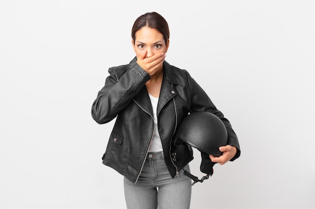 Mujer hispana joven que cubre la boca con las manos con una sorpresa. concepto de piloto de moto