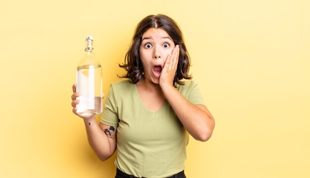 Mujer hispana joven que se siente conmocionada y asustada. concepto de botella de agua