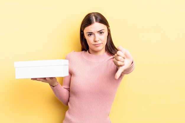 Mujer hispana joven que se siente cruzada, mostrando los pulgares hacia abajo. concepto de caja vacía