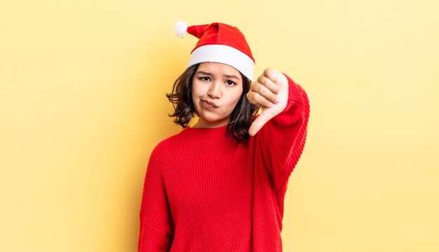 Mujer hispana joven que se siente cruzada, mostrando los pulgares hacia abajo. concepto de navidad