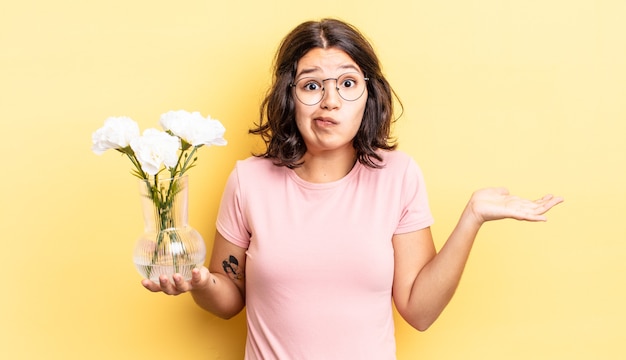 Mujer hispana joven que se siente desconcertado y confundido y dudando. concepto de maceta de flores