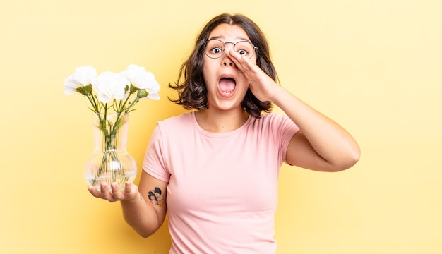 Mujer hispana joven que se siente feliz, dando un gran grito con las manos al lado de la boca. concepto de maceta de flores