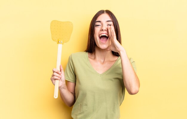 Mujer hispana joven que se siente feliz, dando un gran grito con las manos al lado de la boca. concepto de matar moscas