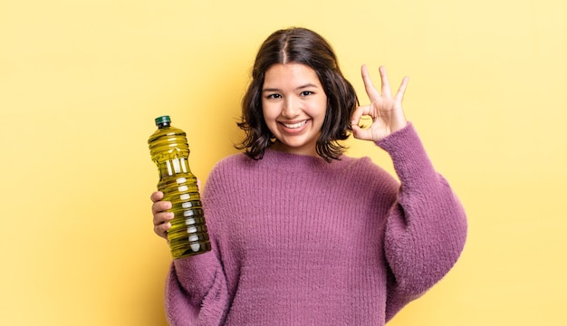 Mujer hispana joven que se siente feliz, mostrando aprobación con gesto bien. concepto de aceite de oliva