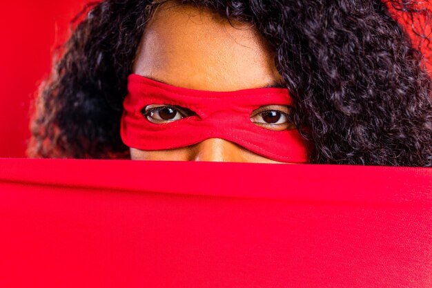 Mujer hispana latina con máscara de ojos rojos y capa larga de superhéroe en el fondo del estudio