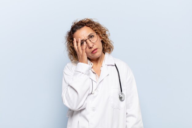 Mujer hispana de mediana edad que se siente aburrida, frustrada y con sueño después de una tarea aburrida, aburrida y tediosa, sosteniendo la cara con la mano