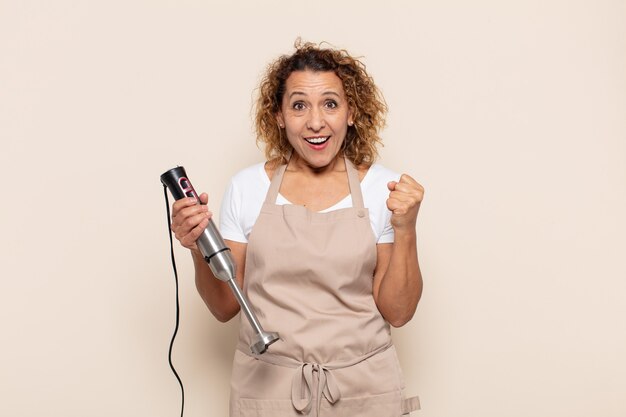 Mujer hispana de mediana edad que se siente sorprendida, emocionada y feliz, riendo y celebrando el éxito, diciendo ¡guau!