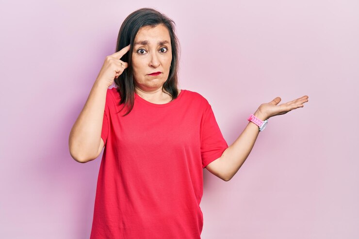 Foto mujer hispana de mediana edad con ropa informal confundida y molesta con la palma abierta mostrando espacio de copia y señalando con el dedo a la frente piénsalo