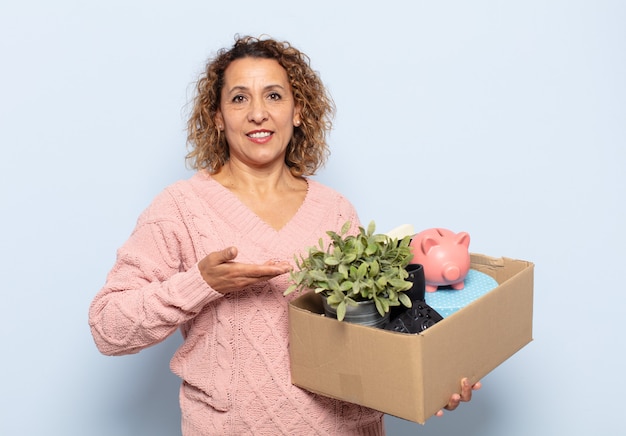 Mujer hispana de mediana edad sonriendo alegremente, sintiéndose feliz y mostrando un concepto en el espacio de la copia con la palma de la mano