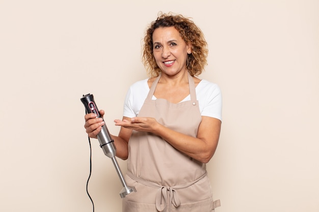 Mujer hispana de mediana edad sonriendo alegremente, sintiéndose feliz y mostrando un concepto en el espacio de la copia con la palma de la mano