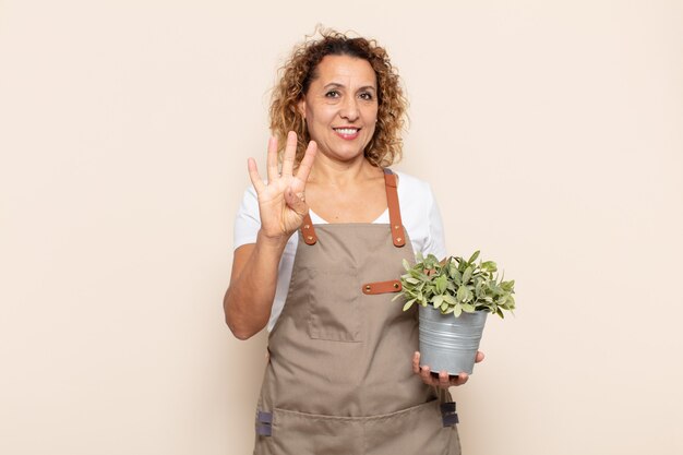 Mujer hispana de mediana edad sonriendo y mirando amistosamente, mostrando el número cuatro o cuarto con la mano hacia adelante, contando hacia atrás