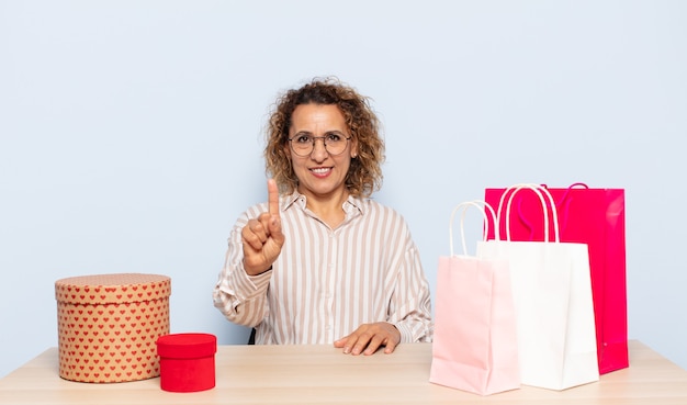 Mujer hispana de mediana edad sonriendo y mirando amistosamente, mostrando el número uno o el primero con la mano hacia adelante, contando hacia atrás