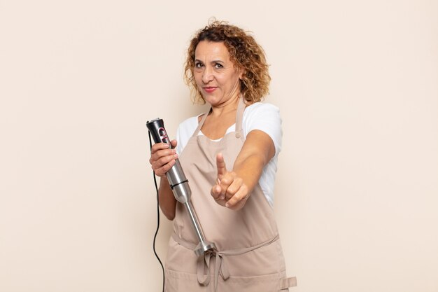 Mujer hispana de mediana edad sonriendo con orgullo y confianza haciendo la pose número uno triunfalmente, sintiéndose como un líder