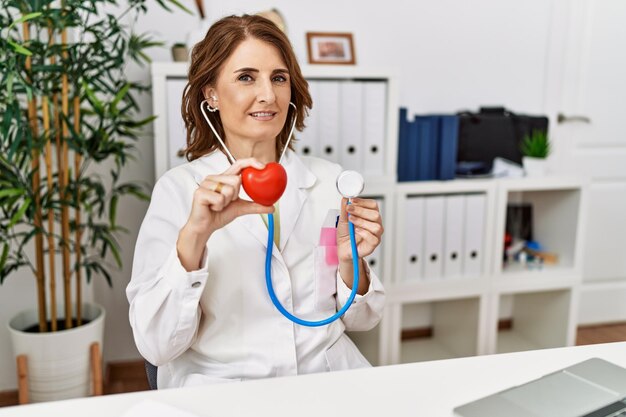 Mujer hispana de mediana edad con uniforme médico auscultando el corazón en la clínica