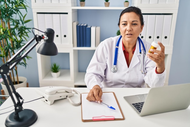 Mujer hispana de mediana edad con uniforme médico prescribe pastillas en la clínica