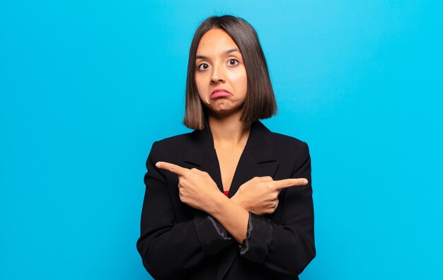 Mujer hispana mirando perpleja y confundida, insegura y apuntando en direcciones opuestas con dudas