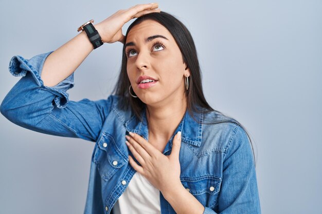 Mujer hispana de pie sobre fondo azul tocando la frente por enfermedad y fiebre, gripe y virus del resfriado enfermo