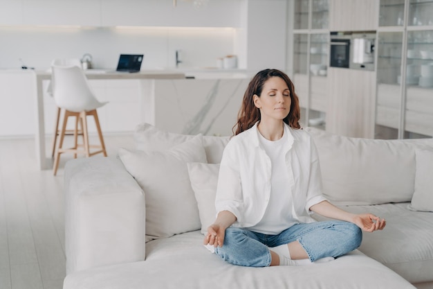 Mujer hispana practicando yoga medita haciendo ejercicios de respiración en un cómodo sofá en casa