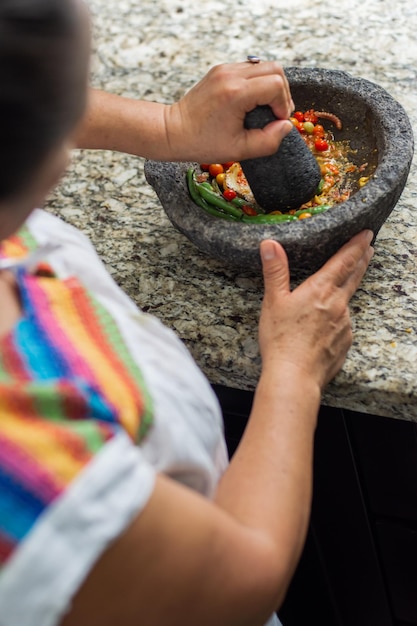 Mujer hispana preparando una salsa picante mexicana con guindilla y tomates en un molcajete
