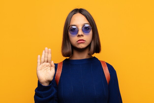 Mujer hispana que parece seria, severa, disgustada y enojada mostrando la palma abierta haciendo gesto de parada