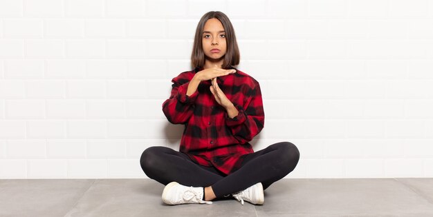 Mujer hispana que parece seria, severa, enojada y disgustada, haciendo el signo de tiempo de espera