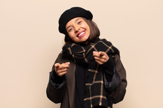 Foto mujer hispana que se siente feliz y segura, apuntando a la cámara con ambas manos y riendo, eligiéndote