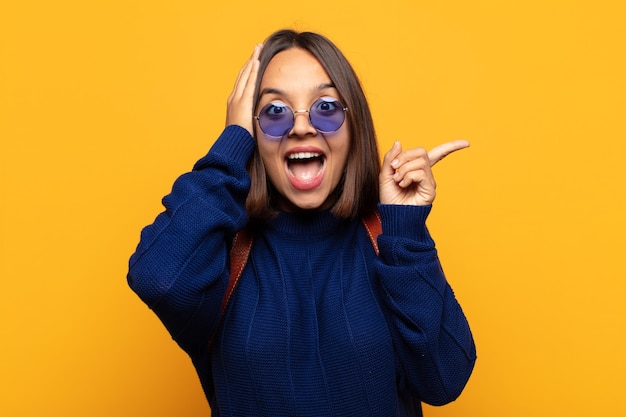 Mujer hispana riendo, luciendo feliz, positiva y sorprendida, dándose cuenta de una gran idea apuntando al espacio de copia lateral