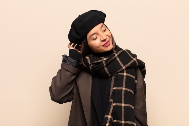 Mujer hispana sonriendo alegre y casualmente, tomando la cabeza con una mirada positiva, feliz y segura